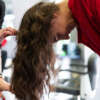 Aged stylist making hairdo to attractive young lady in hairdressing salon