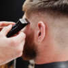 Young bearded man getting haircut by hairdresser while sitting in chair at barbershop. Barber soul.