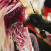 A hair colourist applying pink hair colour to a client's long blonde hair.
