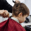 Little boy cut with hairdresser's machine. Close-up of woman hands grooming kid boy hair in barber shop. Start of the haircut. Portrait of male child at the barber shop to cut his hair.