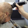 A customer sitting in the barber's chair, and a barber using an electric shaver to shave his head.